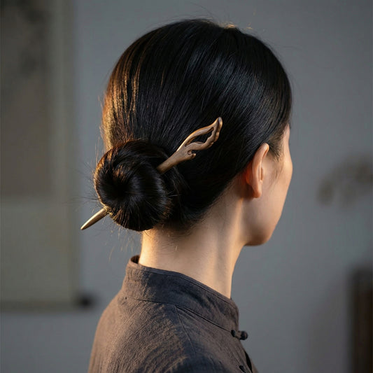 East Asian model wearing Quiet Flame carved wood hair stick in a low bun — rear view showing flame tip and natural sandalwood tone