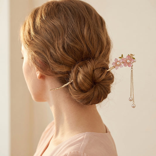 Pink blossom hair stick worn in low bun with pearl chains draping past ear