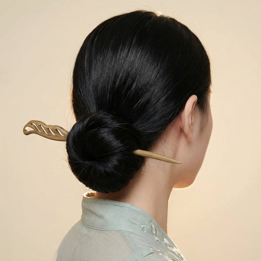 Openwork leaf wood hair stick worn in sleek low bun showing carved cutout detail