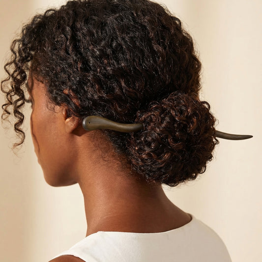 Twisted dark wood hair stick worn in curly low bun showing organic gnarled shape